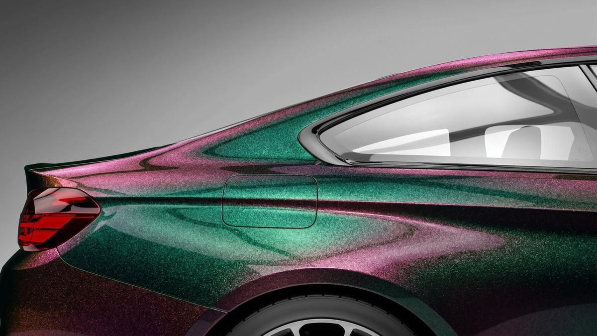 A car's rear three-quarter view finished in colour-shift paint protection film, emerald green blending into magenta across the bodywork against a studio-grey backdrop.